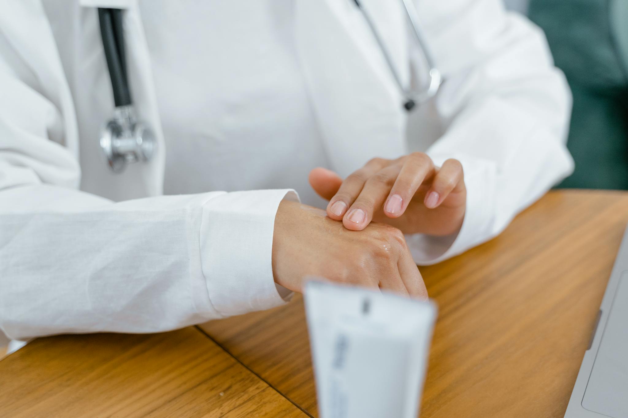 A healthcare professional in a white coat applying cream on hand, emphasizing treatment and care.